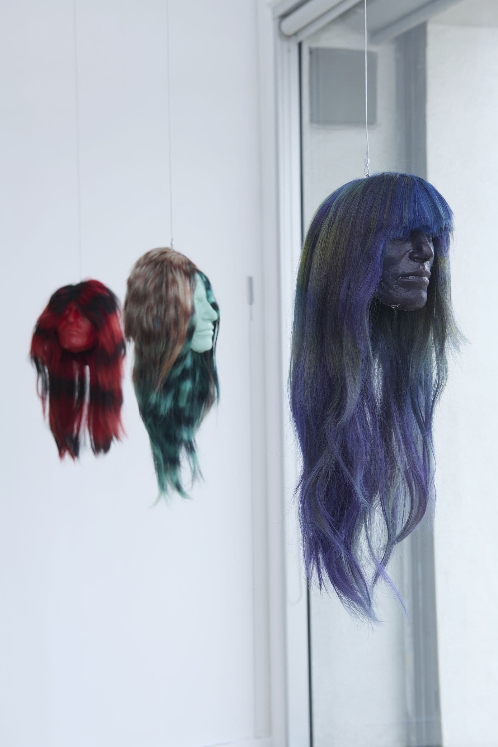 Three suspended hair works lit by the gallery's natural light