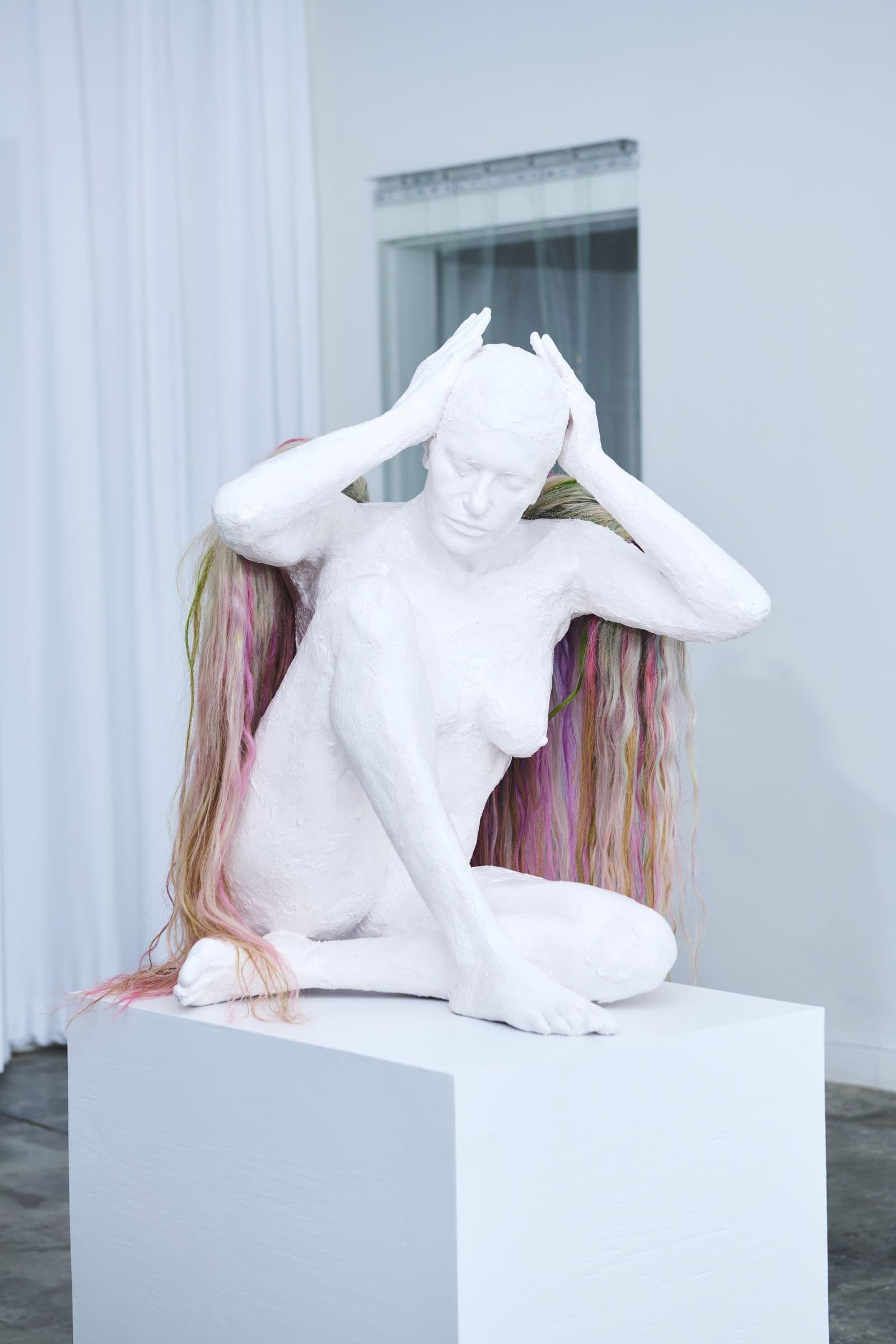 Seated plaster figure with dyed hair on a white plinth