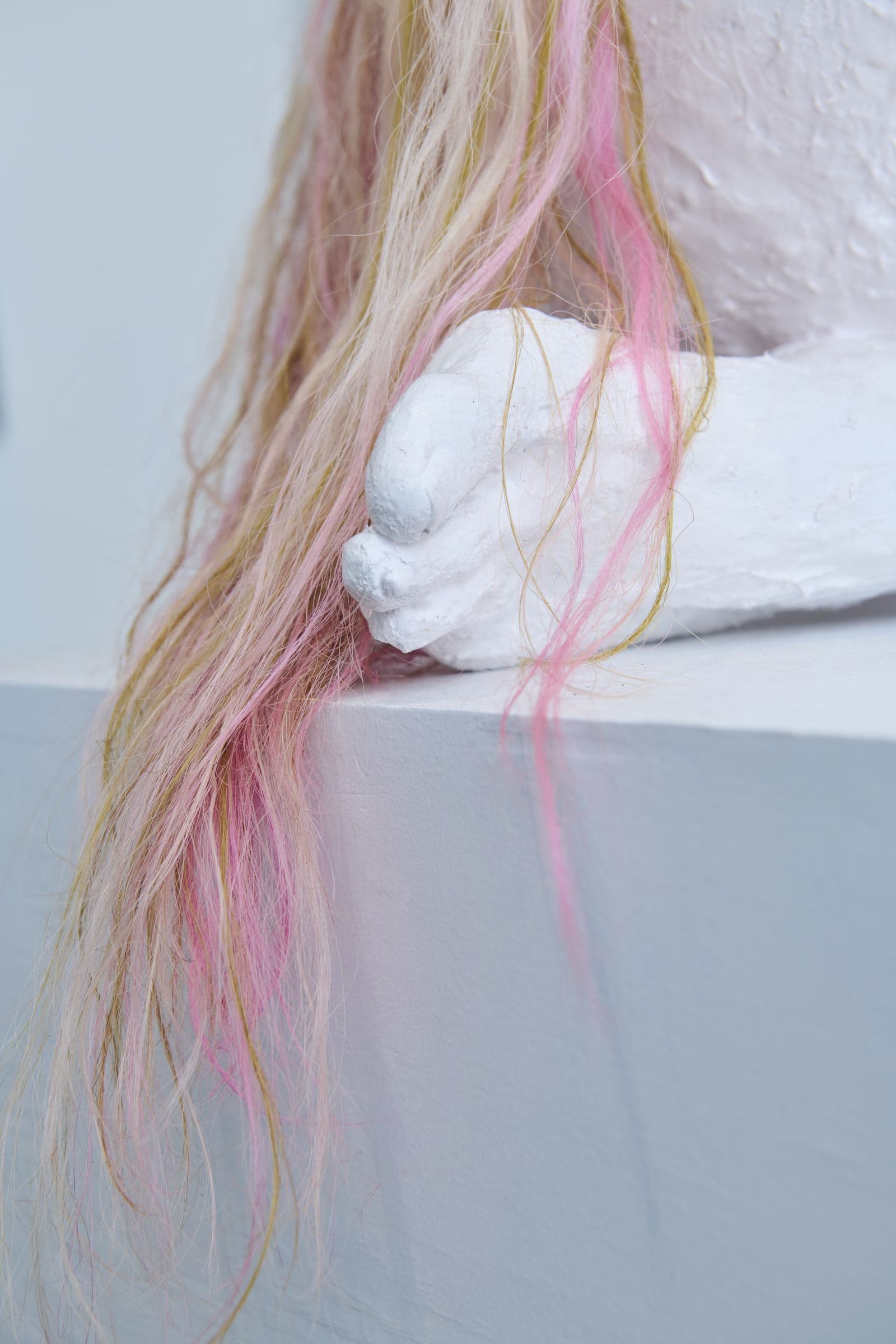 Detail of a plaster hand holding strands of pink hair