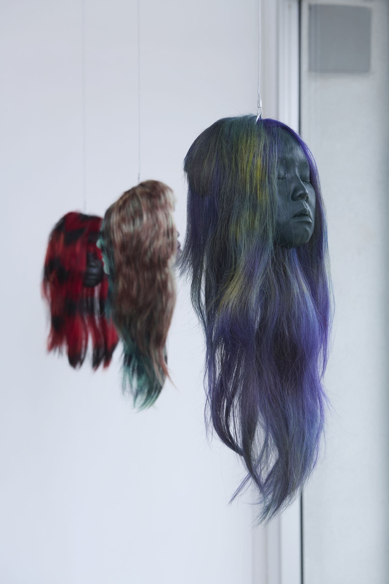 Suspended sculptural hair works beside a gallery mirror