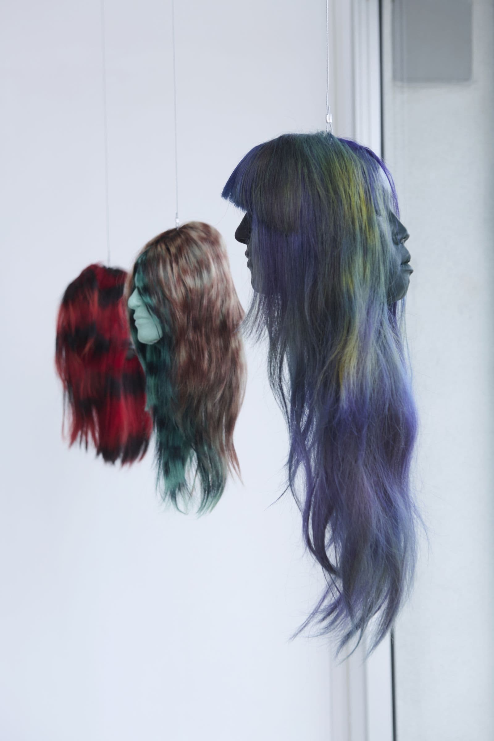 Two suspended sculptural works with dyed hair hanging in the gallery